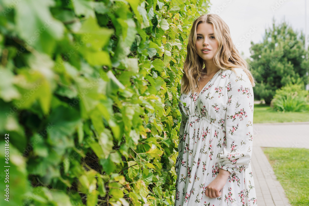 A young beautiful woman in a light dress walks through the park in good summer weather A young beautiful woman in a light dress walks through the park in good summer weather