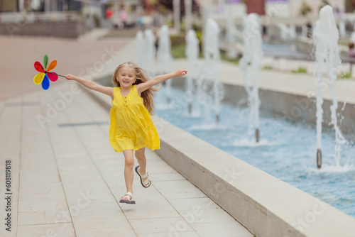 Happy little girl running in the park near the city fountain playing with paper windmill. Summer concept. happy childhood photo