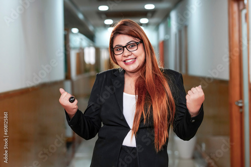 Young corporate woman giving happy and winning gesture at office