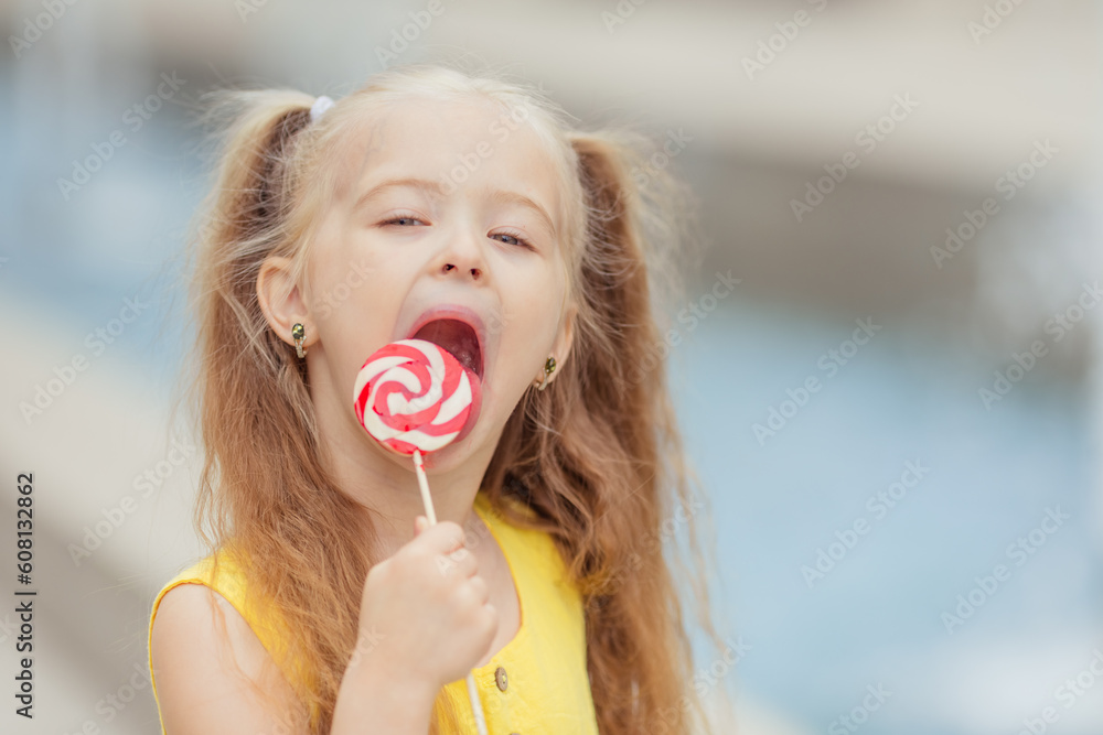 Close up cute little girl walking around the sunny city with lollipop. Summer holidays. Happy childhood
