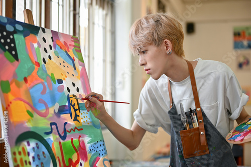 Fototapeta Naklejka Na Ścianę i Meble -  A talented young Asian queer artist focuses on painting his picture on a canvas easel