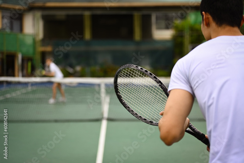 Back view of tennis player standing in ready position to receive a serve, practicing for competition on a court © Prathankarnpap
