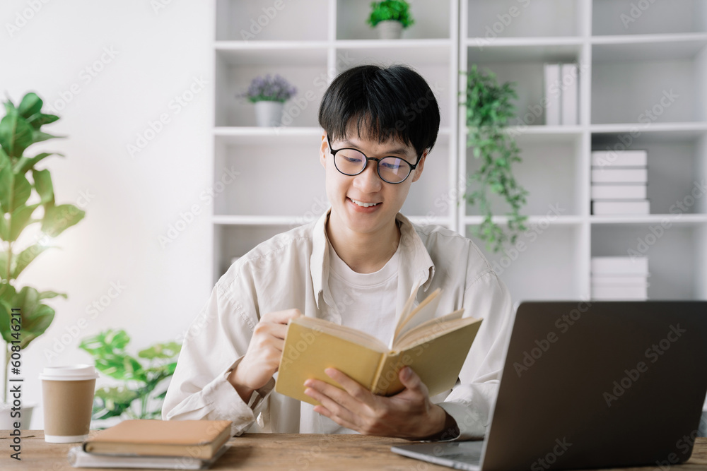 male student in casual clothes sitting at wooden table with laptop and writing notes while preparing for exam in library. male student in casual clothes sitting at wooden table with laptop and writing notes while preparing for exam in library.