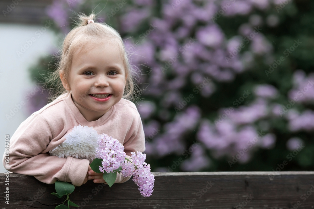 Spring flowering. Portrait of a beautiful little girl 3 years old with lilac flowers in nature. Childhood. The kid poses and looks at the camera.