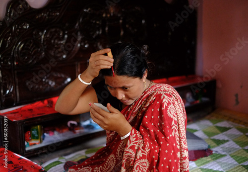 Bengali hindu woman putting sindoor on her forehead as a visual marker of being married, with a belief of well wishes for her husband and as a sign of love  photo