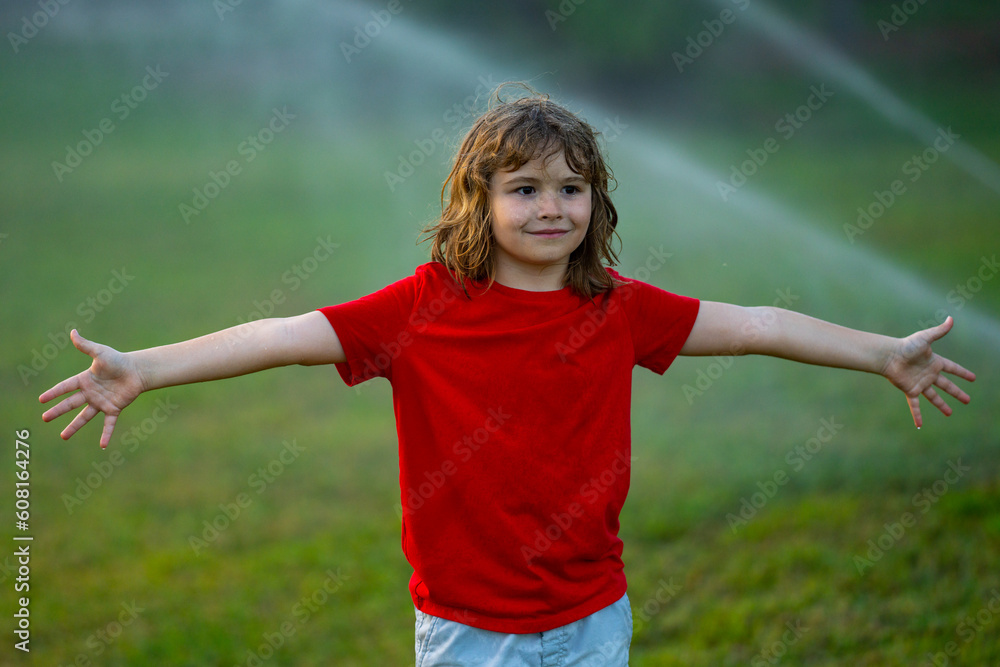 Child play in summer garden. Grass watering. Automatic sprinkler irrigation system in a green park watering lawn. Sprinkler watering. Child gardening concept. Little kid having fun on water spraying.