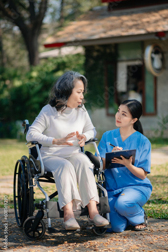 Elderly asian senior woman on wheelchair with Asian careful caregiver and encourage patient, walking in garden. with care from a caregiver and senior