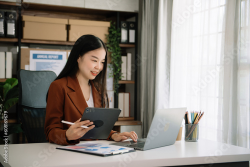 Confident Asian woman with a smile standing holding notepad and tablet at the office.