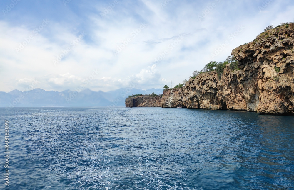 Blue Mediterranean sea, blue sky with white clouds and a rocky shore with a cliff