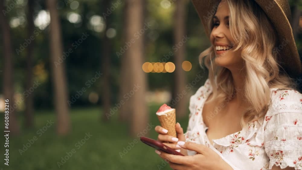 Young attractive woman sitting on bench in city park, using smartphone and eating ice cream, walking on summer sunny day outdoors on vacation Young attractive woman sitting on bench in city park, using smartphone and eating ice cream, walking on summer sunny day outdoors on vacation
