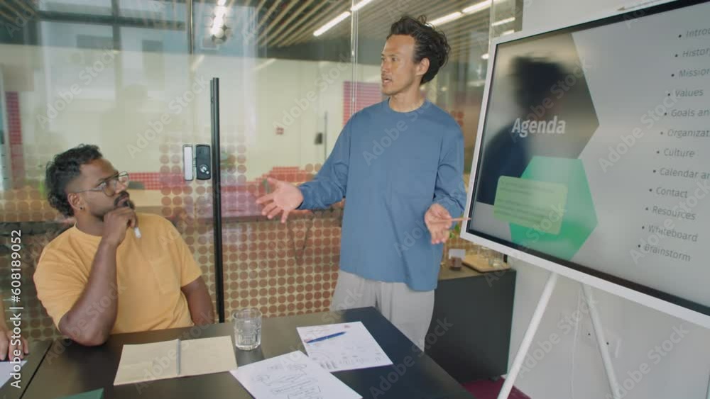 Young Asian man giving business presentation on digital screen to coworkers and answering questions during office meeting Young Asian man giving business presentation on digital screen to coworkers and answering questions during office meeting
