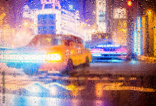 View through a glass window with raindrops on a blurred silhouette of a people walking on autumn rain , night street scene. focus on raindrops 