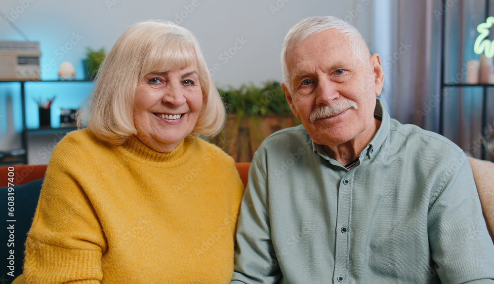 Happy old senior elderly family couple hugging, laughing, smiling looking at camera, healthy retired two grandparents husband wife. Grandmother grandfather embracing sitting on sofa at home, portrait Happy old senior elderly family couple hugging, laughing, smiling looking at camera, healthy retired two grandparents husband wife. Grandmother grandfather embracing sitting on sofa at home, portrait