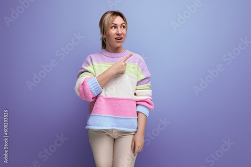 blond girl in surprise shows her hand to the side on a purple background with copy space © Ivan Traimak