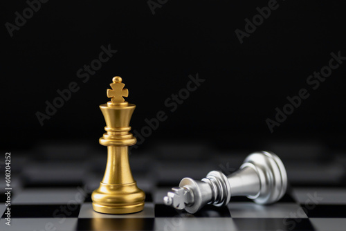 Golden king chess standing and silver king chess falling on chess board.