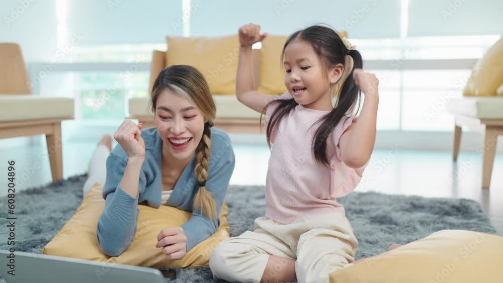 Happy asian mother and little daughter joy raising hands while looking at laptop receive good news message, celebrate win in living room at home. Lifestyle technologies Happy asian mother and little daughter joy raising hands while looking at laptop receive good news message, celebrate win in living room at home. Lifestyle technologies