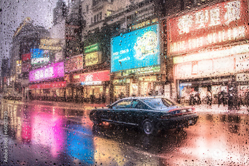 View through a glass window with raindrops on city streets with cars in the rain, bokeh of colorful city lights, night street scene. Focus on raindrops on glass © Павел Мещеряков