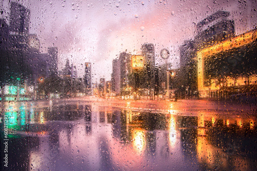View through a glass window with raindrops on city streets with cars in the rain, bokeh of colorful city lights, night street scene. Focus on raindrops on glass © Павел Мещеряков
