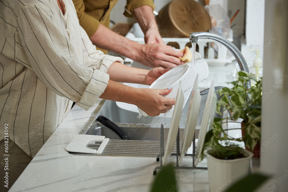 Fototapeta premium Cropped image of couple rinsing plates under tap water after having dinner at home