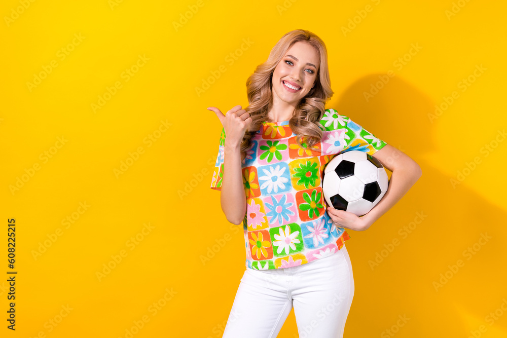 Photo of sweet cute lady wear flower print t-shirt holding football ball thumb empty space isolated yellow color background Photo of sweet cute lady wear flower print t-shirt holding football ball thumb empty space isolated yellow color background