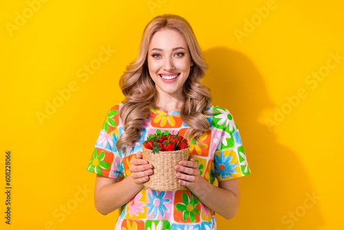 Photo of friendly adorable positive nice girl dressed colorful t-shirt hold basket with strawberry isolated on yellow color background