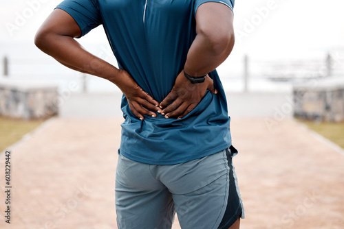 Man, fitness and back pain after workout, cardio exercise or running and training outdoors. Rear view of male person, athlete or runner with sore spine, injury or ache and bone inflammation in nature