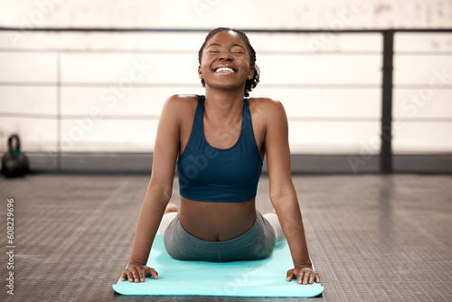 Happy black woman, yoga and stretching body at gym for healthy exercise, workout or cardio training. African female person or yogi with smile in warm up stretch or svanasana pose on mat for fitness photo