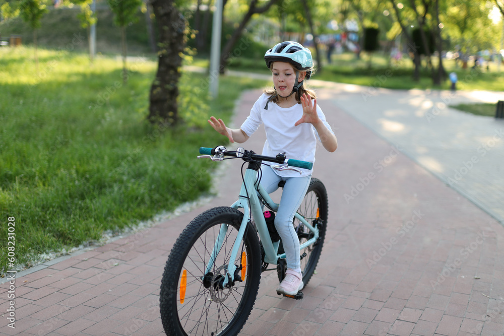 A cheerful little girl in a helmet is trying to ride a bicycle without hands. A cheerful little girl in a helmet is trying to ride a bicycle without hands.