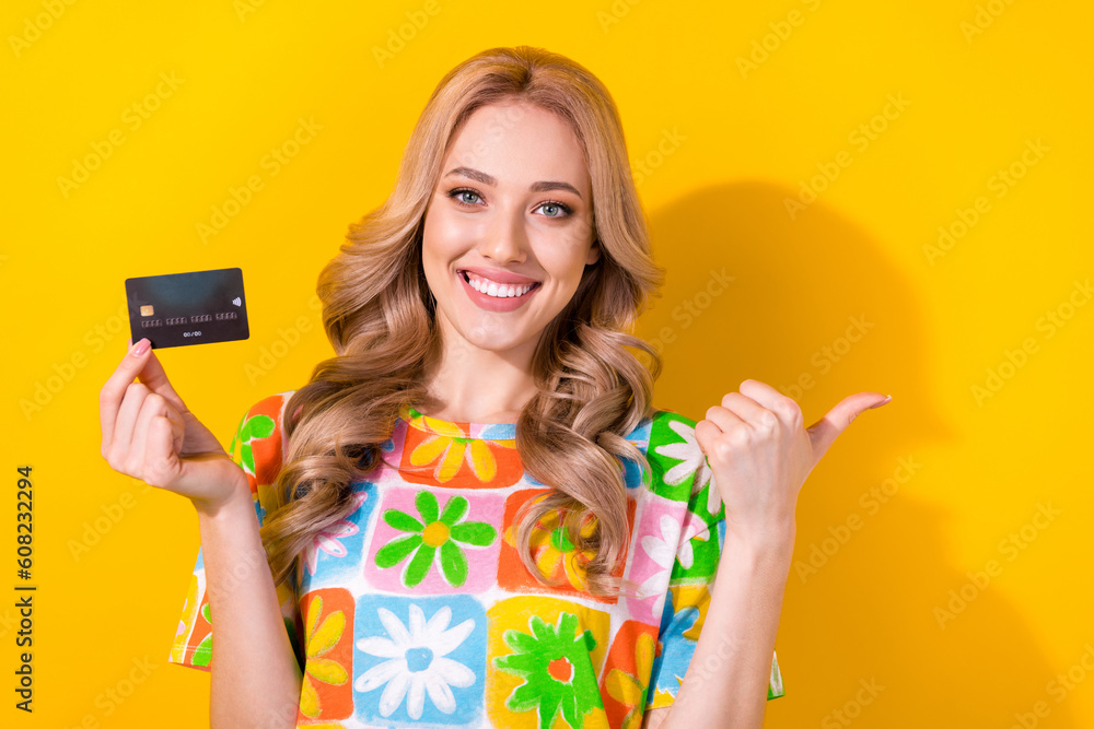 Photo of satisfied girl dressed colorful t-shirt hold plastic card directing at sale empty space isolated on yellow color background Photo of satisfied girl dressed colorful t-shirt hold plastic card directing at sale empty space isolated on yellow color background