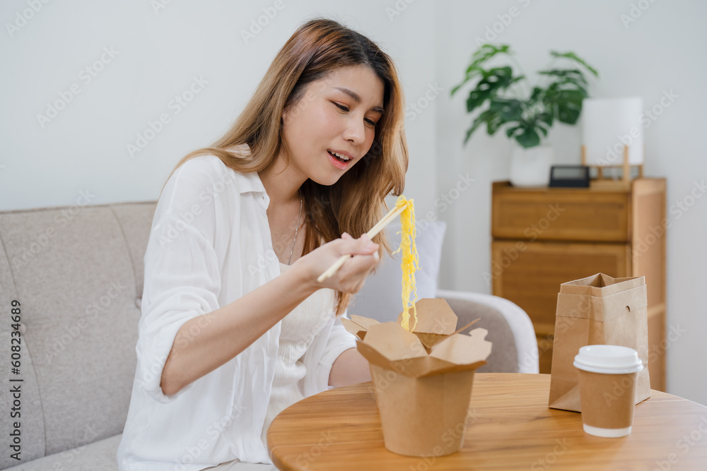 Food delivery. Happy asian woman eating noodles with chopsticks unpacking takeaway food at home. Food delivery. Happy asian woman eating noodles with chopsticks unpacking takeaway food at home.