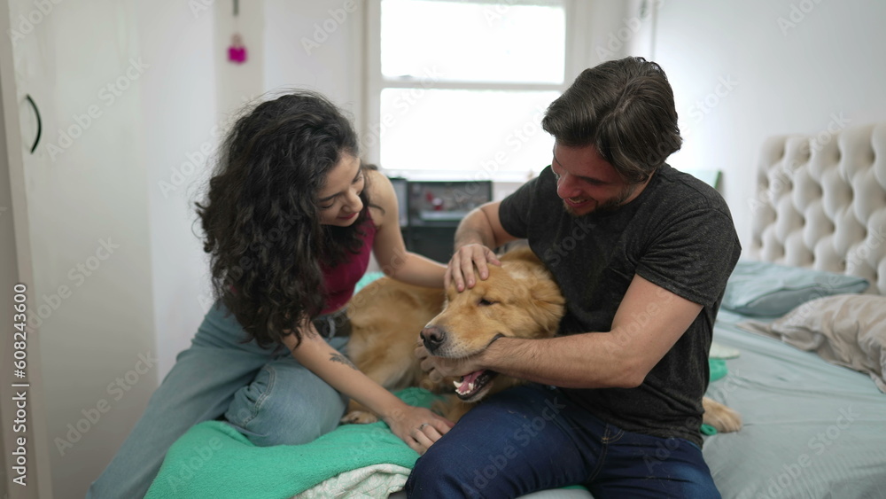 Couple playing with Dog at home sitting on bed. Young man and woman interacting with their Golden Retriever Pet