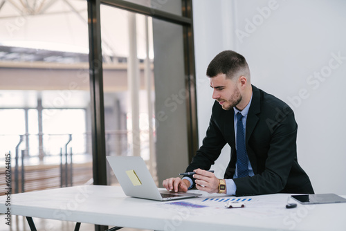 A caucasian male using laptop working at office. Car salesman planning to manage transportation finance costs. Dealership and online sales concept.