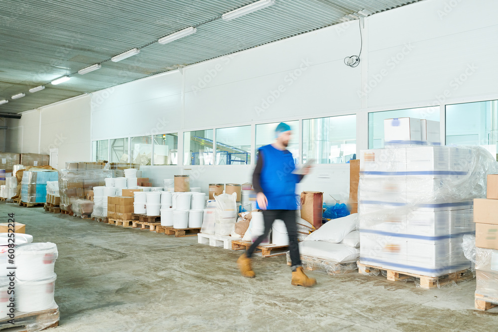 Blurred motion of busy warehouse manager in uniform reading online records on tablet while hurrying to shipment station Blurred motion of busy warehouse manager in uniform reading online records on tablet while hurrying to shipment station