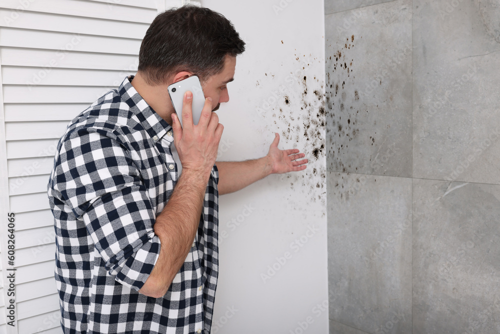 Obraz premium Mold removal service. Man talking on phone and looking at affected walls in room