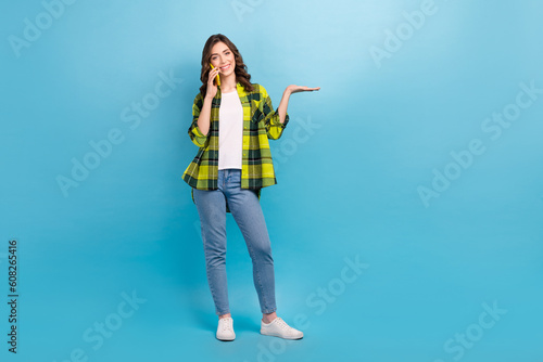 Full body photo of charming cheerful lady speak communicate telephone arm hold empty space isolated on blue color background