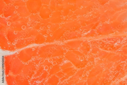 Close-up of a grapefruit slice in liquid with bubbles. Slice of ripe grapefruit in water. Close-up of fresh grapefruit slice covered by bubbles. Macro horizontal image.