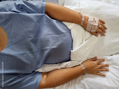 Top view two hands of woman patient with a stick tube of saline solution in a hospital room.