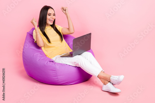 Full length photo of cute lucky lady wear yellow t-shirt sitting bean bag winning game device empty space isolated pink color background