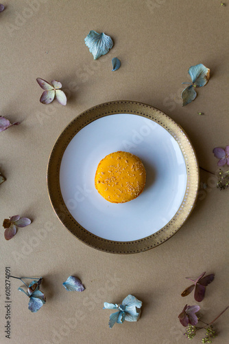 Orange macaron on a white and golden plate, against a neutral beige background with dried blooms