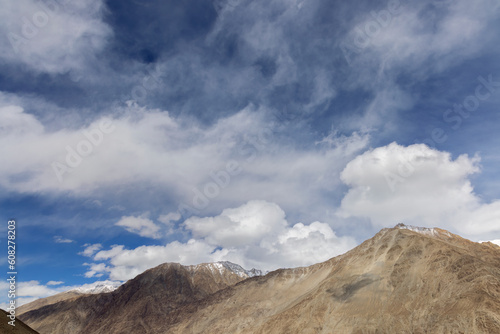 Explore the stunning Leh and Ladakh region, where the endless blue sky meets towering mountains, adorned with fluffy clouds, offering a mesmerizing and scenic view of nature's beauty.
