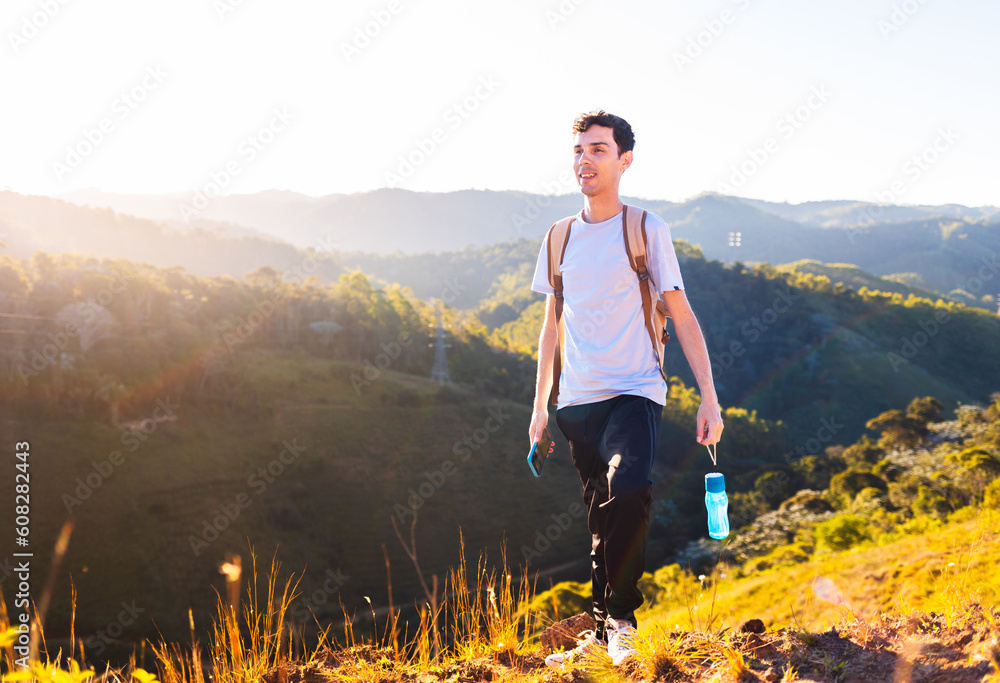Happy man walking high up on a mountain for exercise and relaxation while carrying a water bottle.