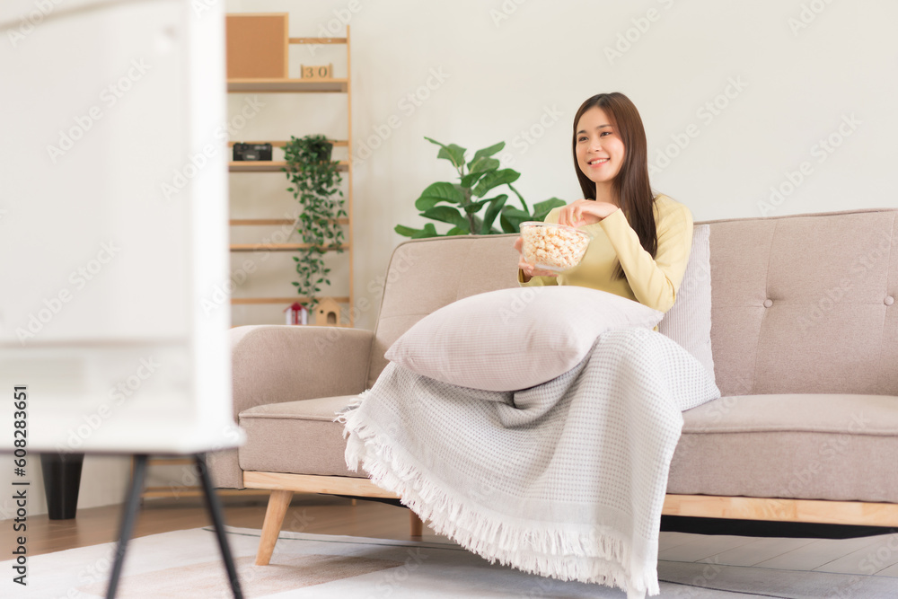 Leisure activity concept, Young woman eating popcorn while sitting on couch to watching television Leisure activity concept, Young woman eating popcorn while sitting on couch to watching television