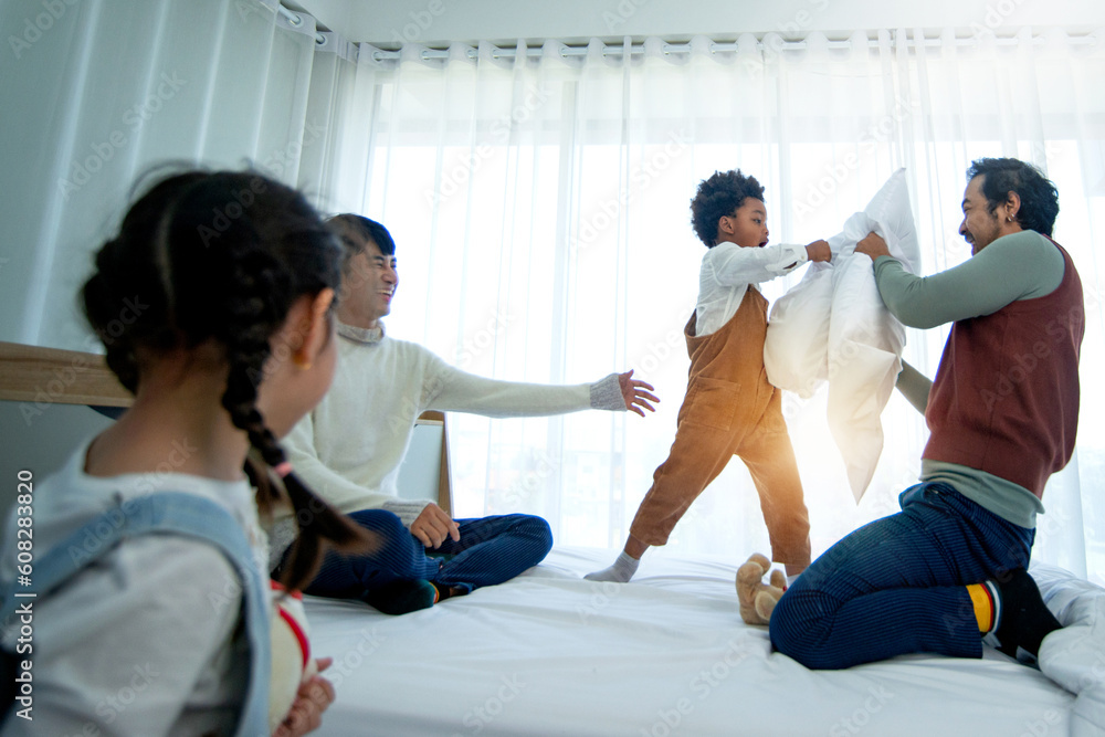 Fototapeta premium LGBTQ family, Male gay couple having fun with daughter and son on bed, fighting with pillows, pillows war on bed