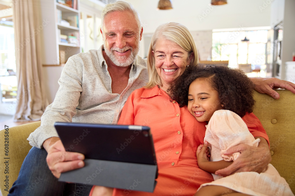 Granddaughter And Grandparents On Sofa At Home Making Video Call On Digital Tablet