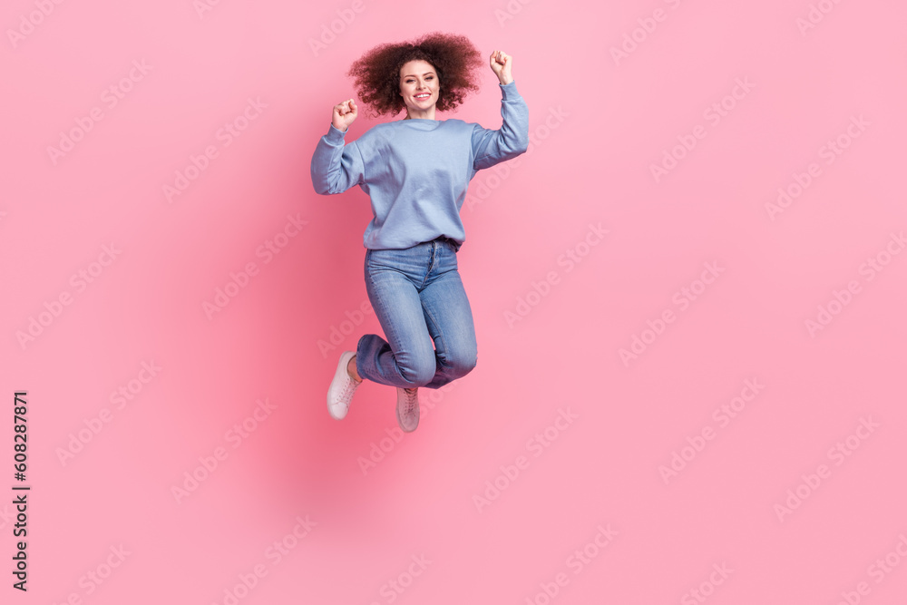 Full length photo of funky lucky lady wear blue sweatshirt jumping high rising fists empty space isolated pink color background