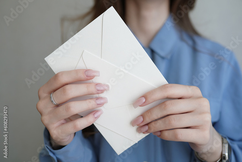 Women's hands hold two milk-colored envelopes. One small, the second large envelope. The concept of invitation to the wedding, bachelorette party, birthday. Mock up with empty space.