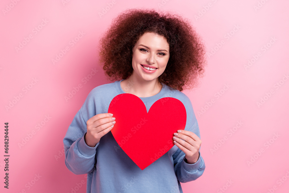 Photo of shiny adorable lady wear blue sweatshirt holding red heart card isolated pink color background Photo of shiny adorable lady wear blue sweatshirt holding red heart card isolated pink color background