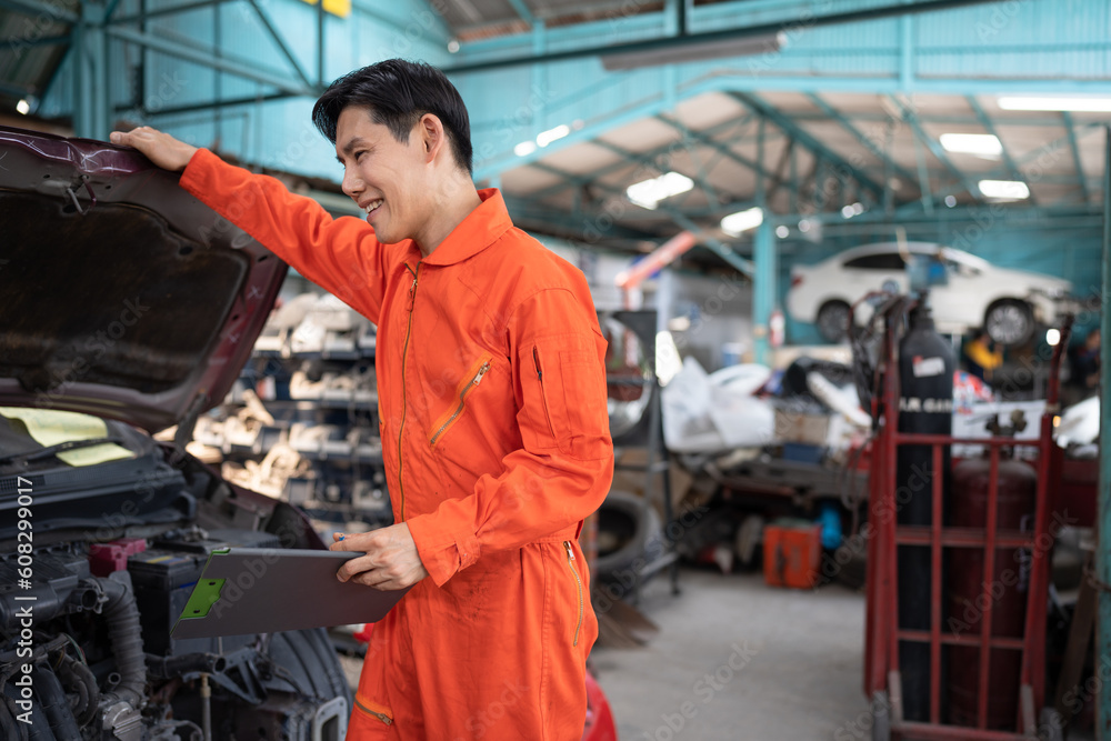 Asia mechanic man examining and maintenance to engine a vehicle car hood with car lift background at car service	
