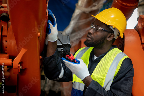 Black Froman chief man holding walkie-talkie discussing repair parts for a robotic arm in an industrial factory.
