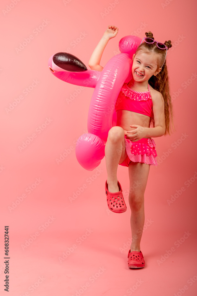 Happy joyful child girl in swimsuit having fun with swimming ring flamingo on a colored pink background. Summer beach concept Happy joyful child girl in swimsuit having fun with swimming ring flamingo on a colored pink background. Summer beach concept